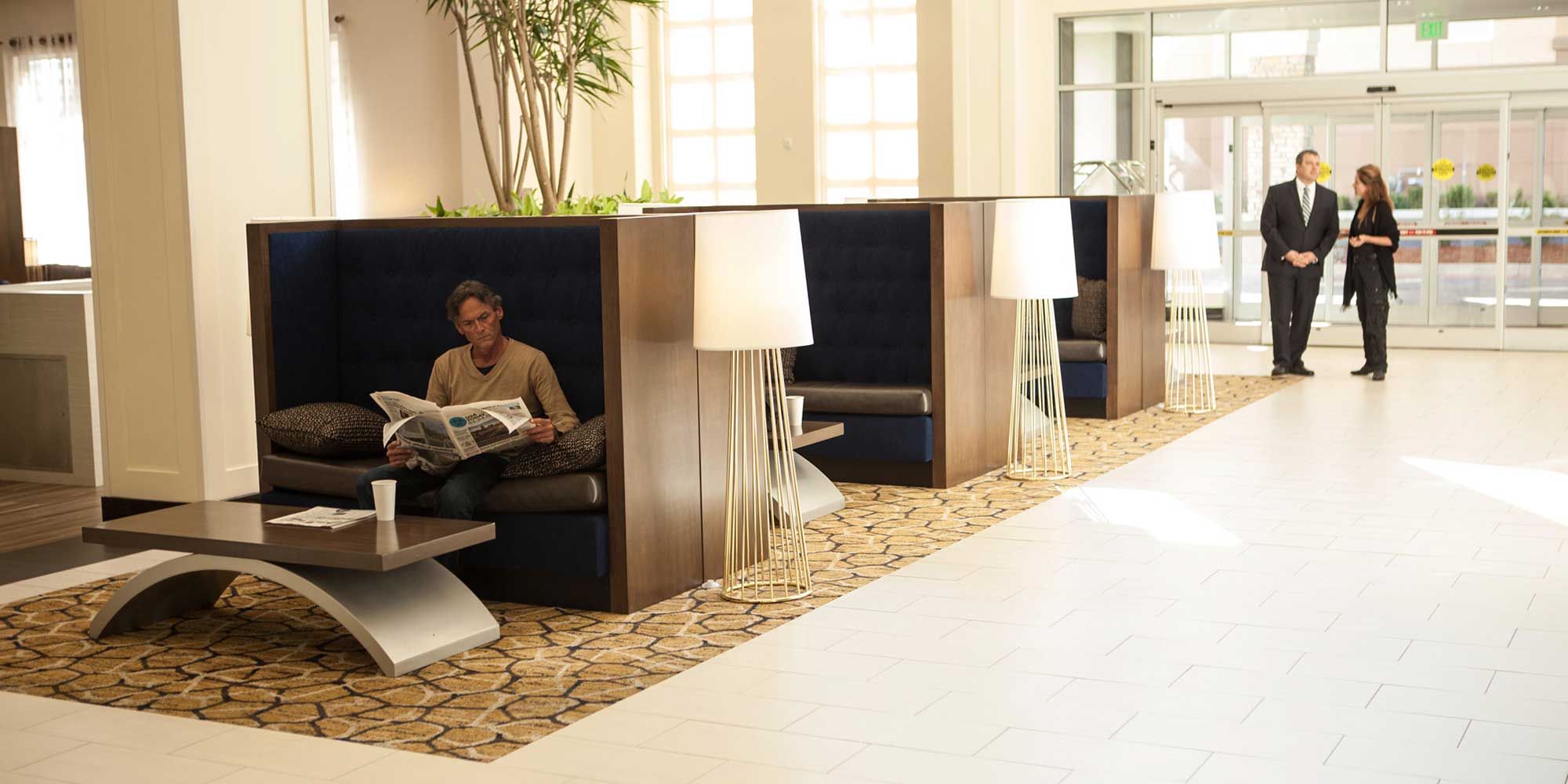 workers having a discussion and a man reading a newspaper in a hotel lobby