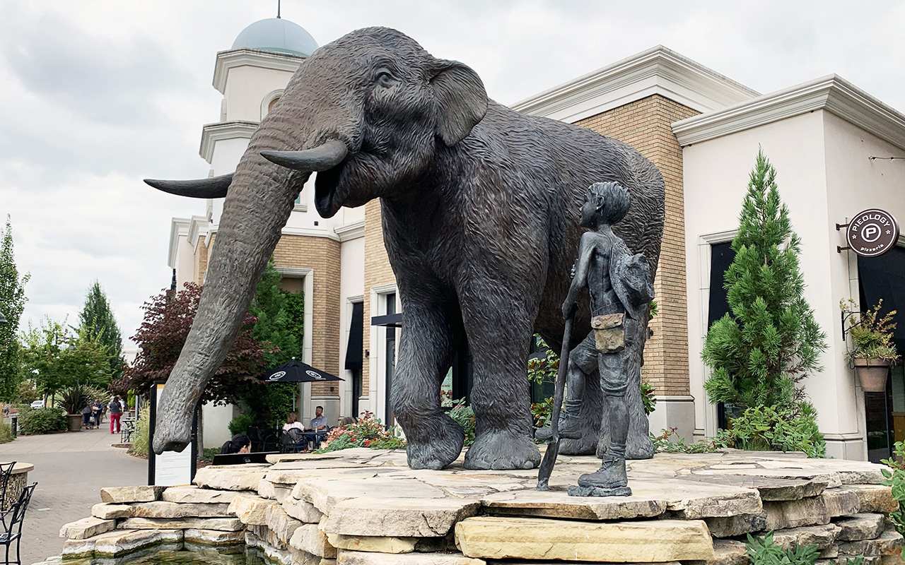 bronze statue of a boy looking at a mastodon