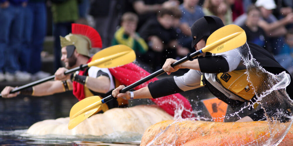 two competitors paddling in pumpkins in a race on a lake