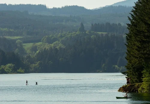 Two people on paddle boards and a kayaker on Henry Hagg Lake with the backdrop of mountains and forests